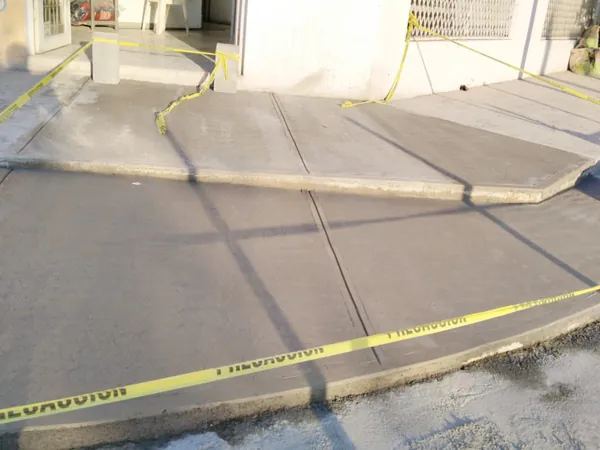 Firme de concreto recién colado en banqueta y acceso vehicular con cinta de precaución