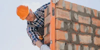 Albañil con casco verificando la plomada de un muro de tabique con un nivel